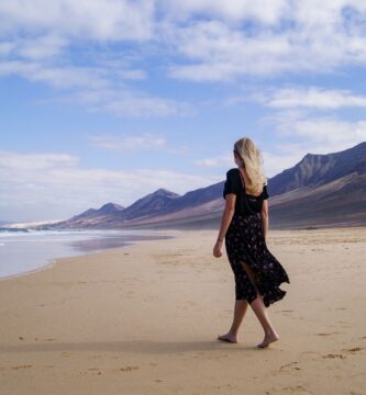 Mujer caminando por la playa de Cofete con las montañas de Jandía al fondo, en Fuerteventura