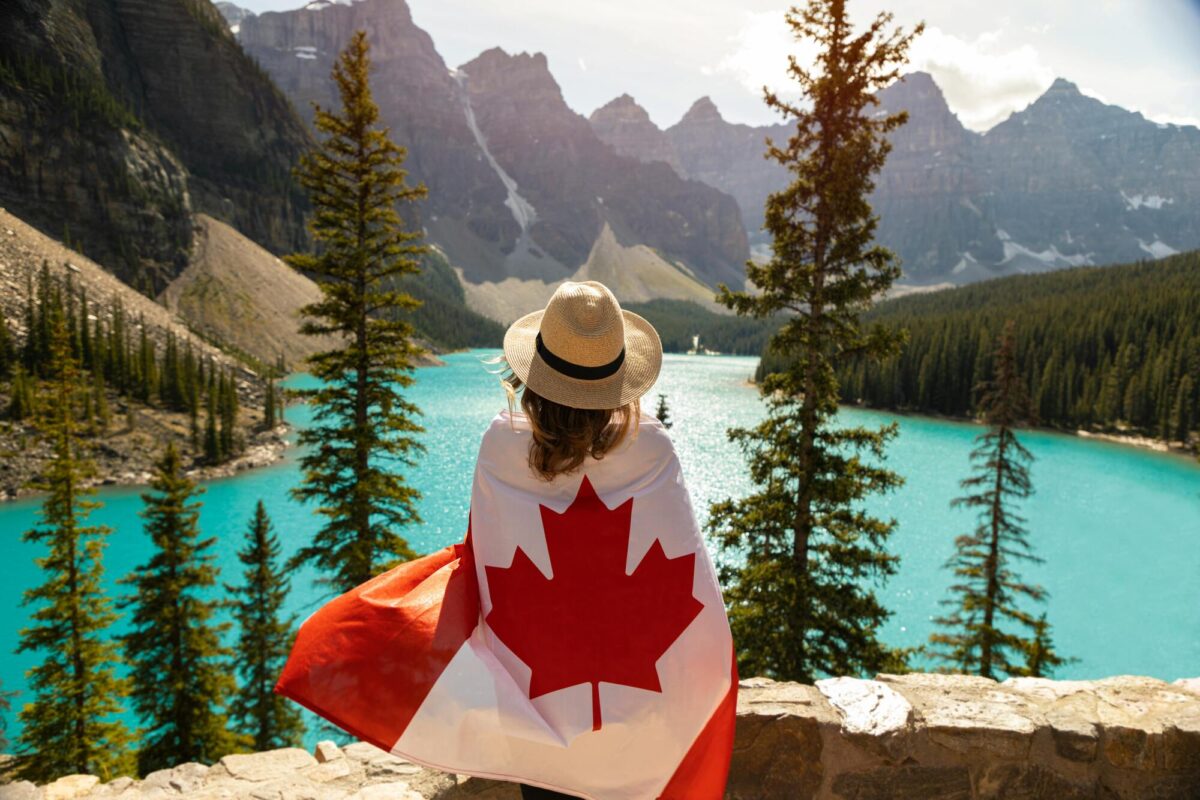 Una mujer con la bandera de Canadá frente a un paisaje del país