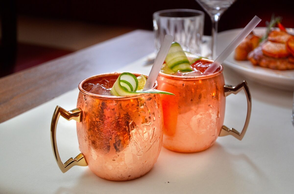Dos cócteles con hielo, lima y pepino servidos en vasos de cobre