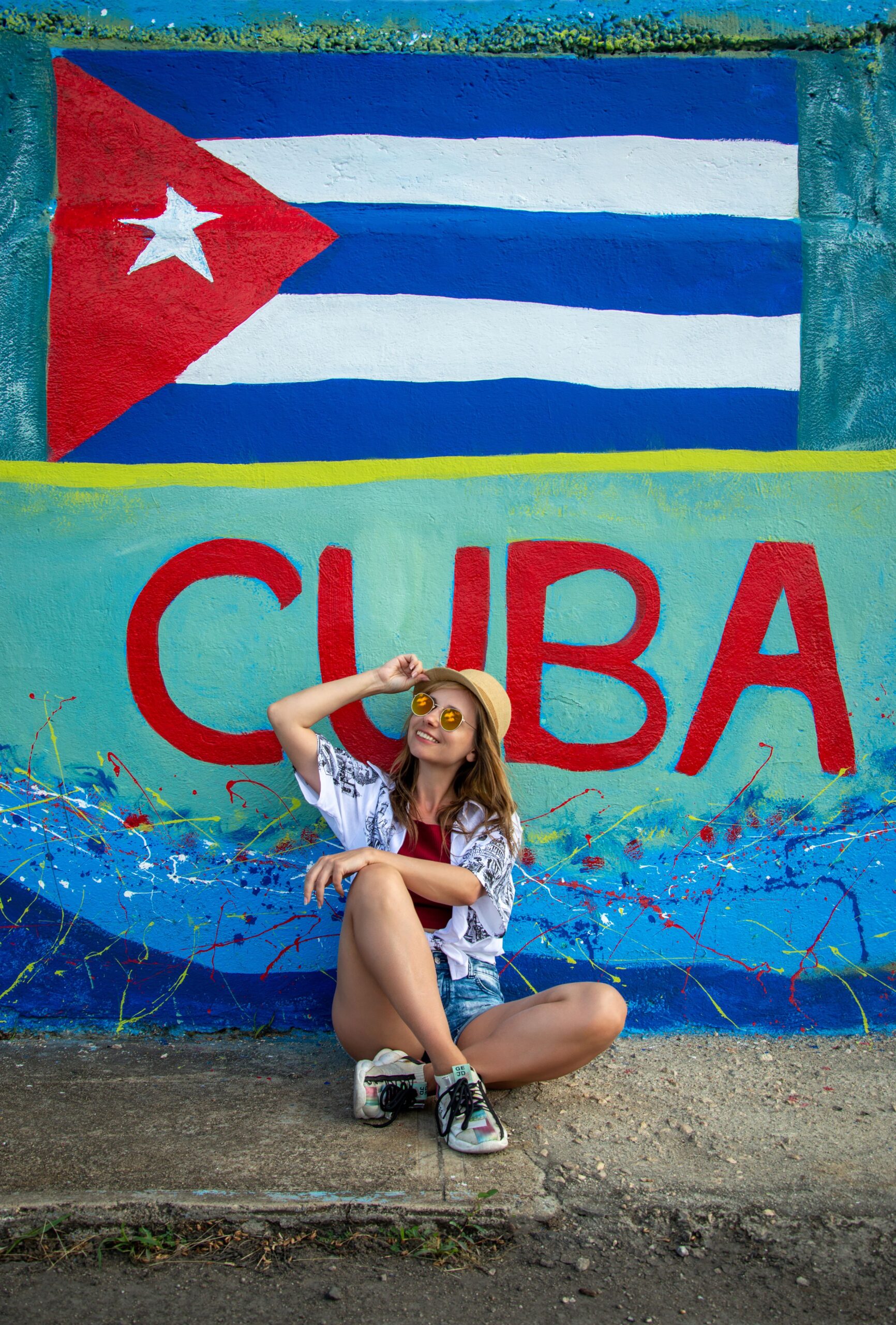 Turista junto a un mural de Cuba Turista sentada frente a un mural con la bandera de Cuba
